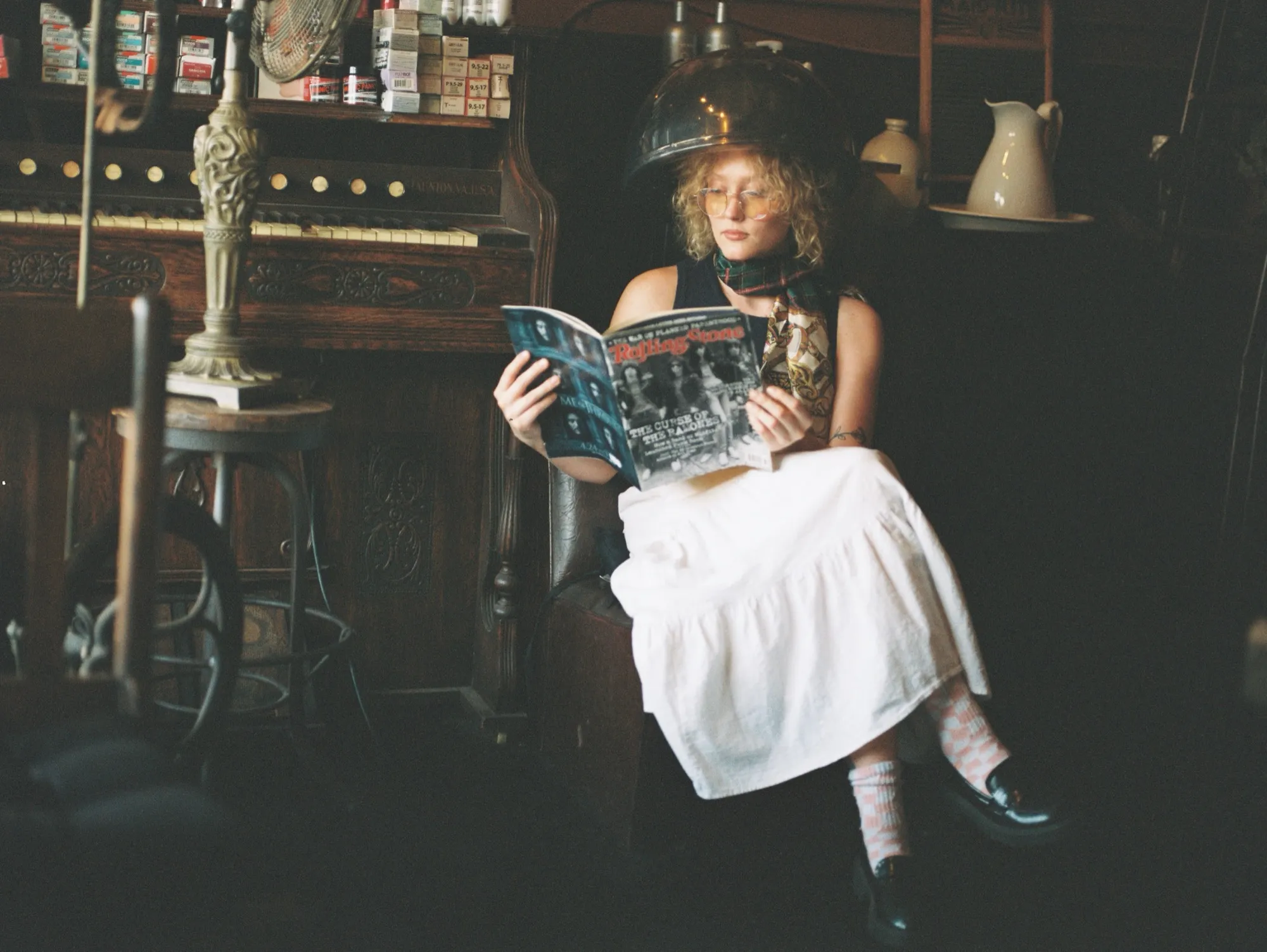 L.A.Z.I.E sitting under a vintage salon hair dryer in an antique shop, reading a magazine